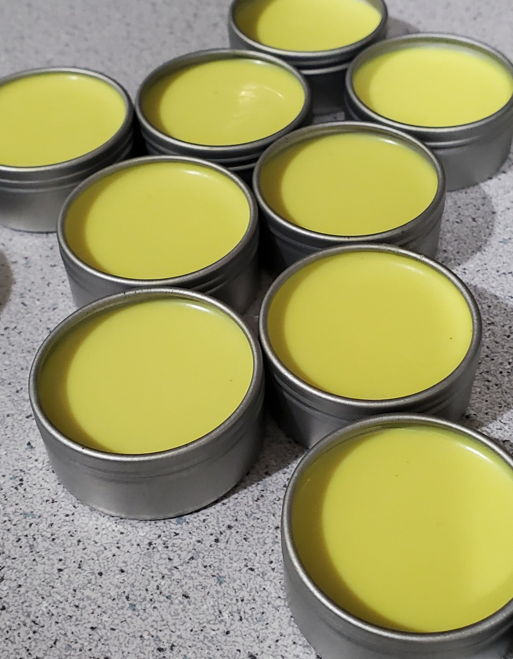 Small metal tins with open lids containing yellow-colored balm.