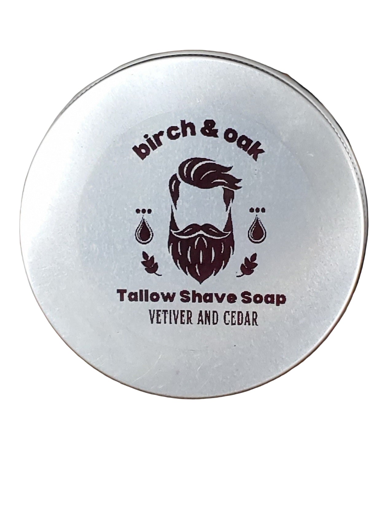 A round tin container with a lid, featuring the 'Birch & Oak' logo and the words 'Tallow Shave Soap Vetiver & Cedar' on it, placed on a wooden surface.