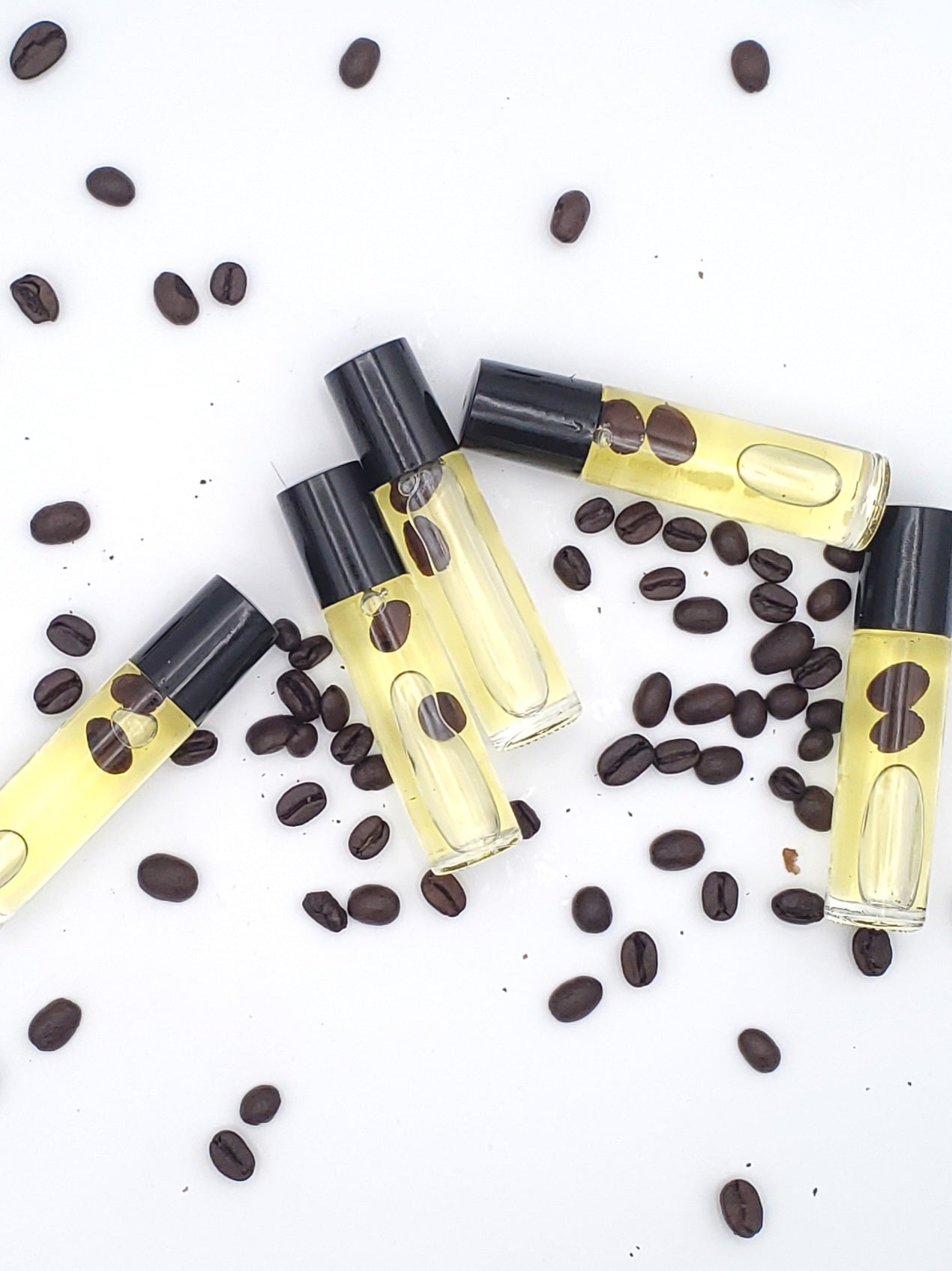 Small glass bottles with black caps, filled with a yellowish liquid, surrounded by coffee beans scattered on a white background.